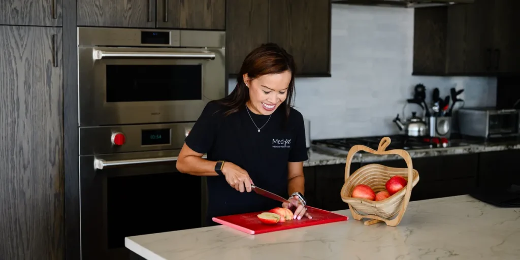 Dr. Angela Tran, DO cutting fruit at her kitchen island beside a basket of apples