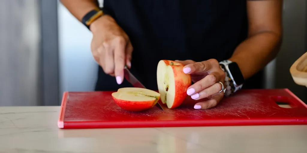 Dr. Angela Tran, DO slicing an apple in half on a red cutting board